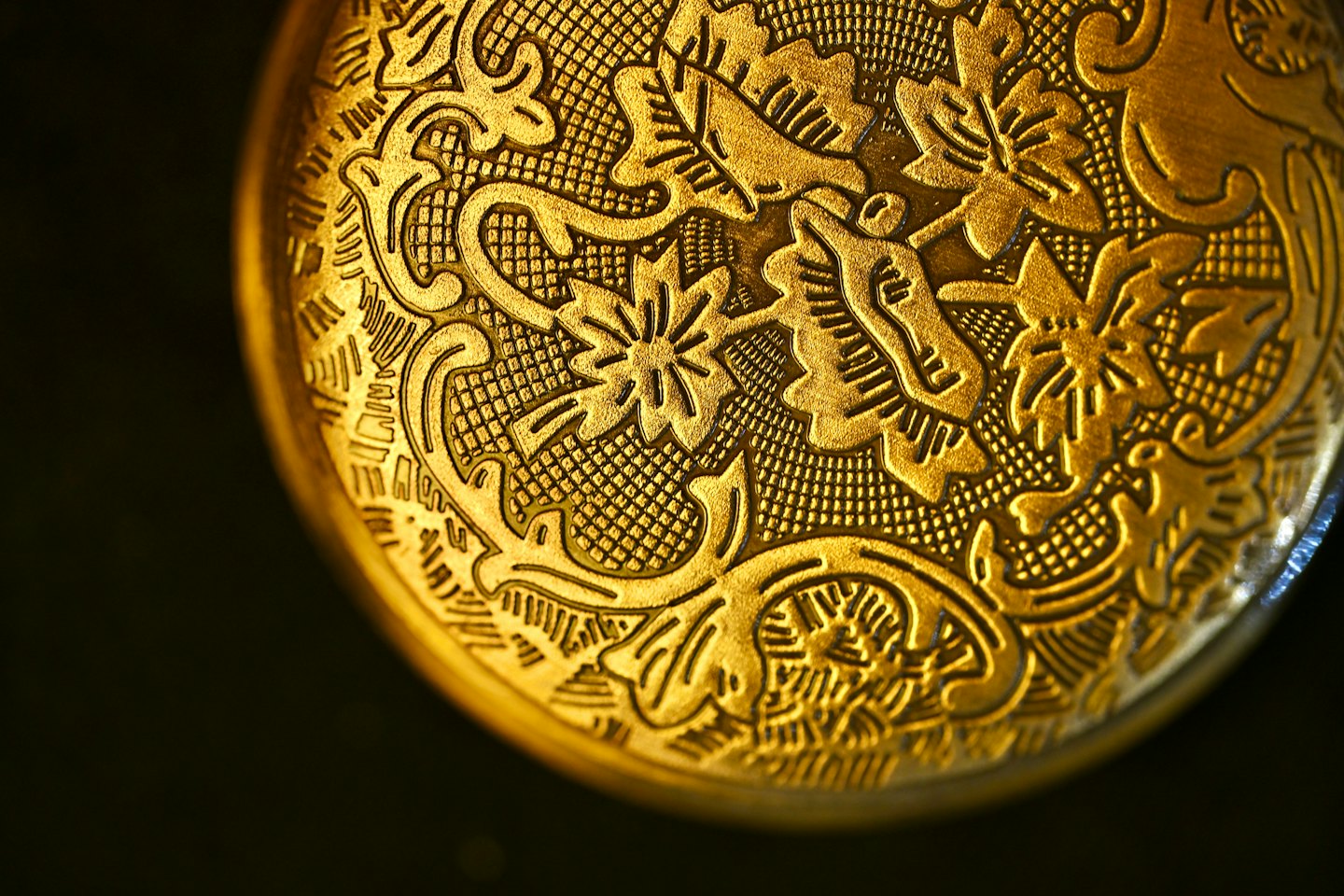 Detailed golden metal surface featuring intricate engraved floral patterns.